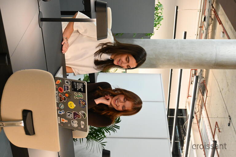 a person sitting at a table with a laptop and smiling at the camera