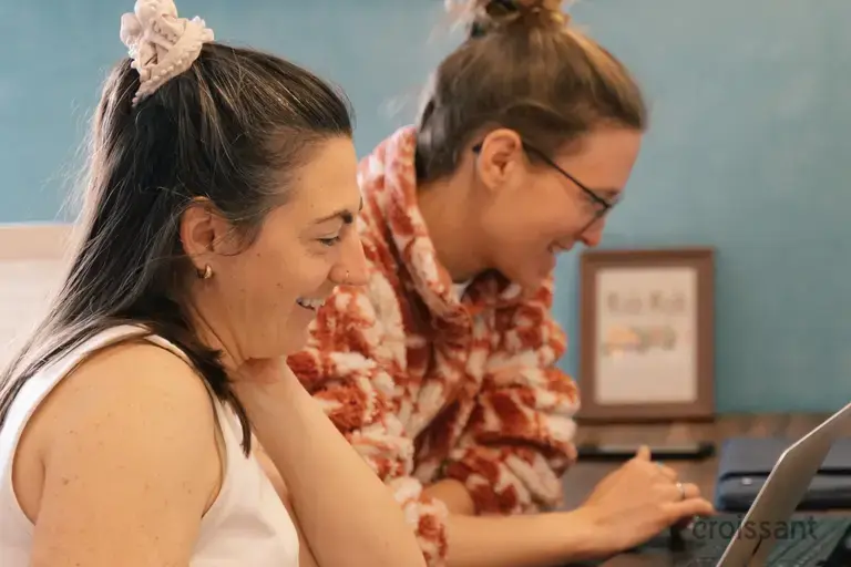 a couple of women sitting at a table looking at a laptop